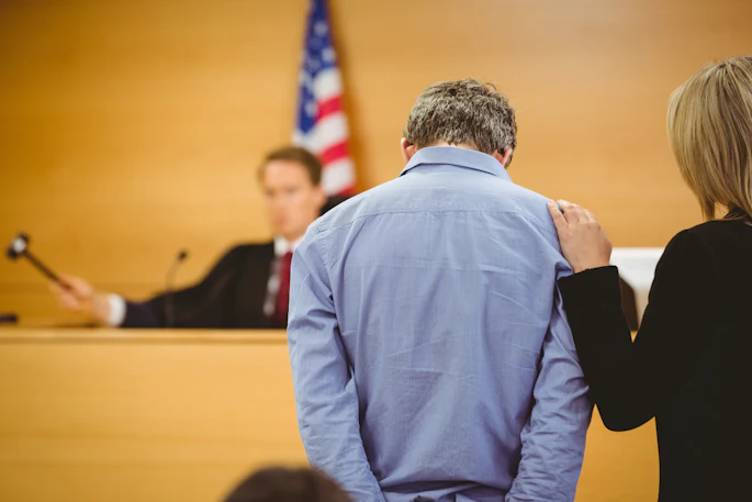 A man hangs his head down, with his hands behind his back, as he appears before a judge.