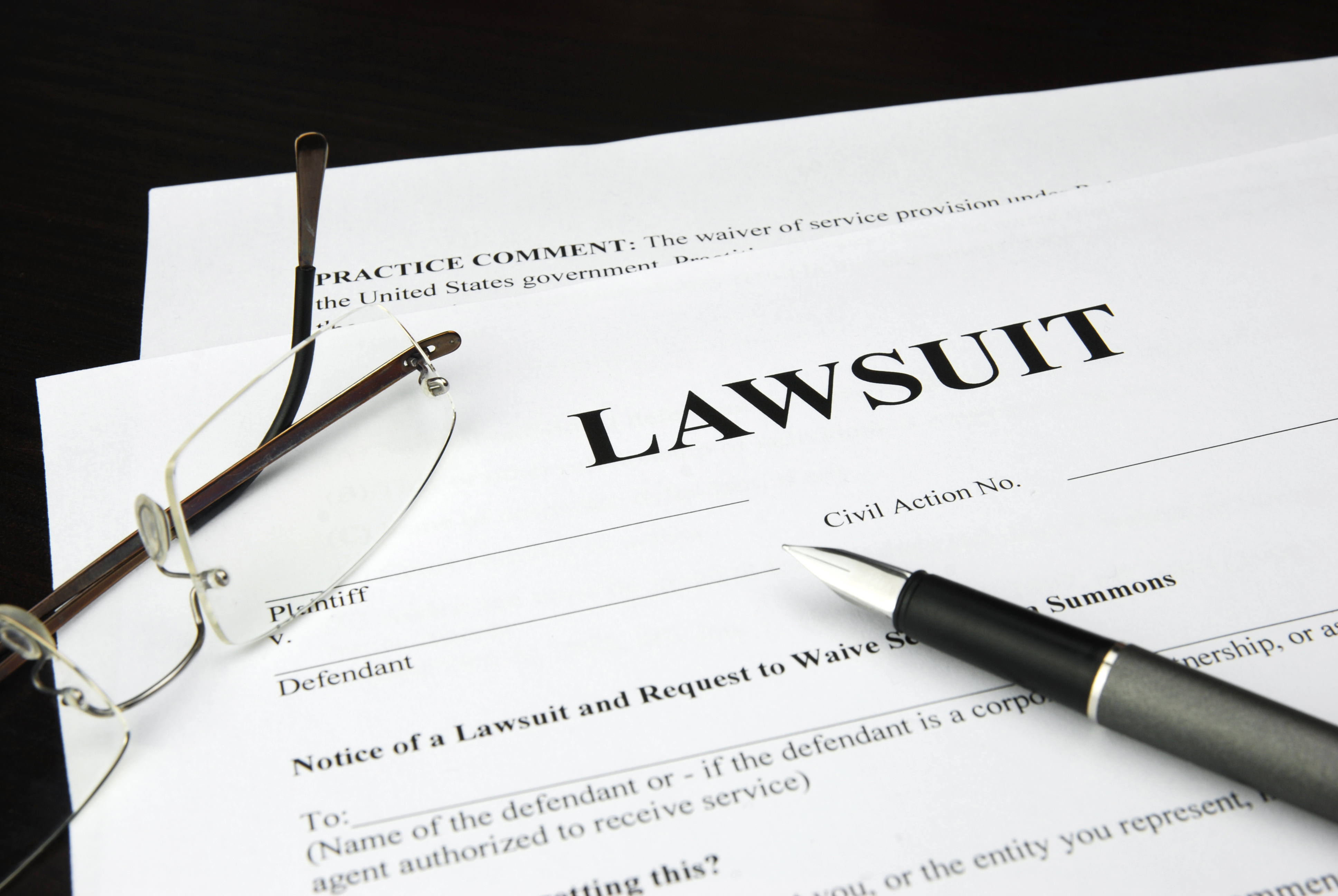 A white document is shown titled 'Lawsuit,' with glasses and a fountain pen resting on top.
