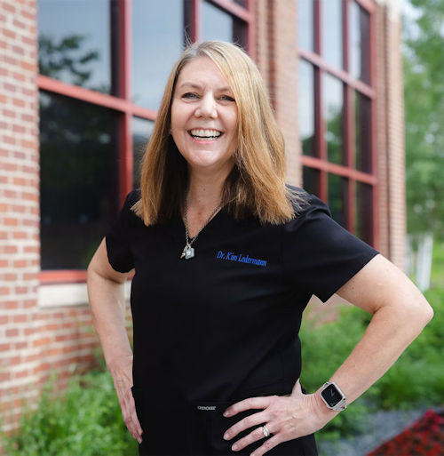 Professional woman in black polo shirt smiling outdoors in front of brick building
