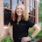 Professional woman in black polo shirt smiling outdoors in front of brick building Headshot