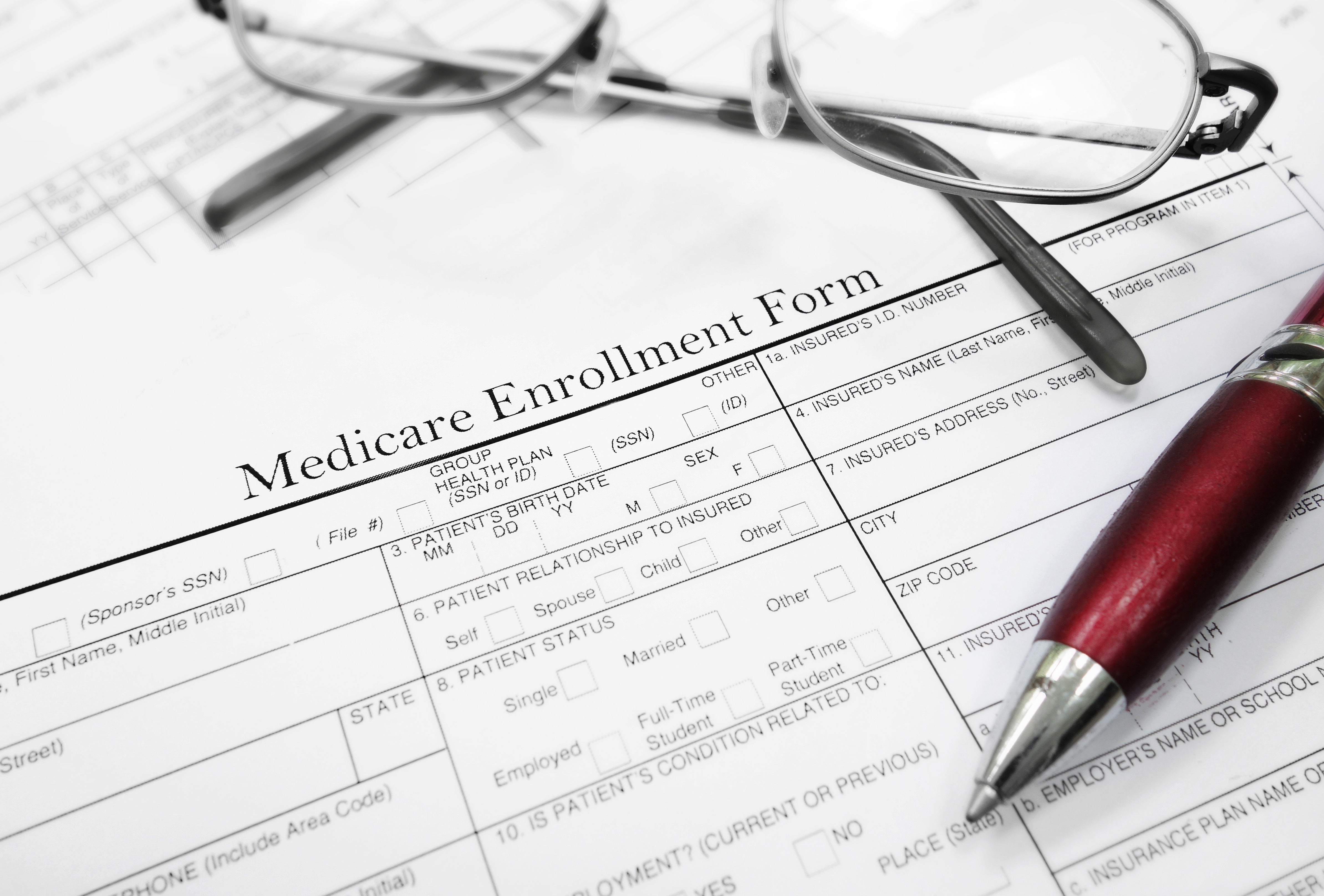 Medicare Enrollment Form with glasses and red pen on desk.