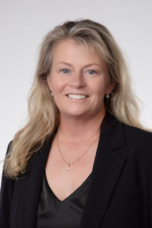 Professional headshot of a smiling woman with long blonde hair wearing a black blazer and cross necklace