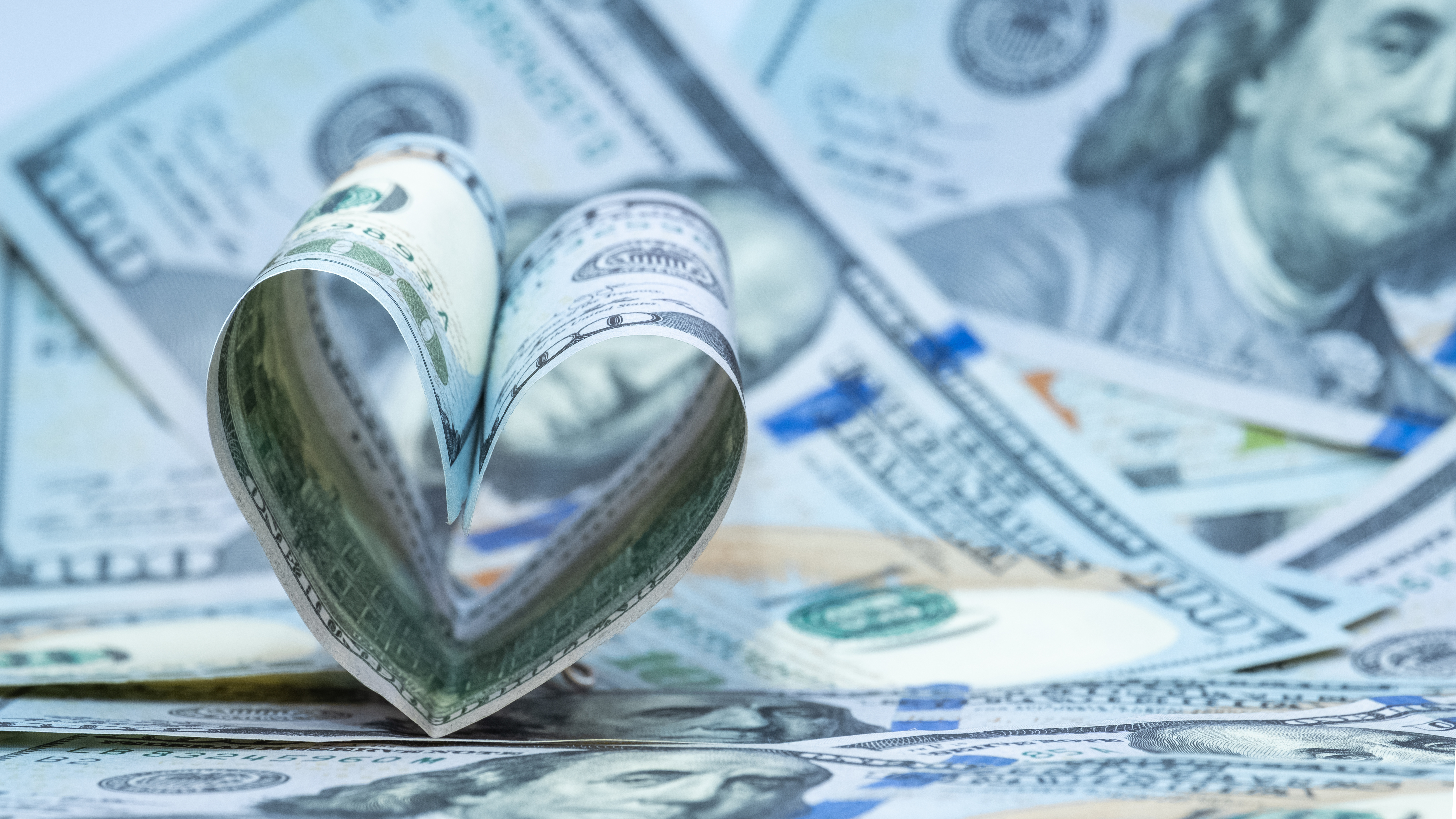 Rolled U.S. dollar bills shaped into a heart on scattered currency, symbolizing financial donation.