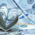 Rolled U.S. dollar bills shaped into a heart on scattered currency, symbolizing financial donation.
