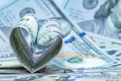 Rolled U.S. dollar bills shaped into a heart on scattered currency, symbolizing financial donation.