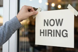 Close-up of a person taping a 'Now Hiring' sign to a glass door.