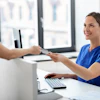 A woman healthcare worker accepts a credit card from a woman patient.