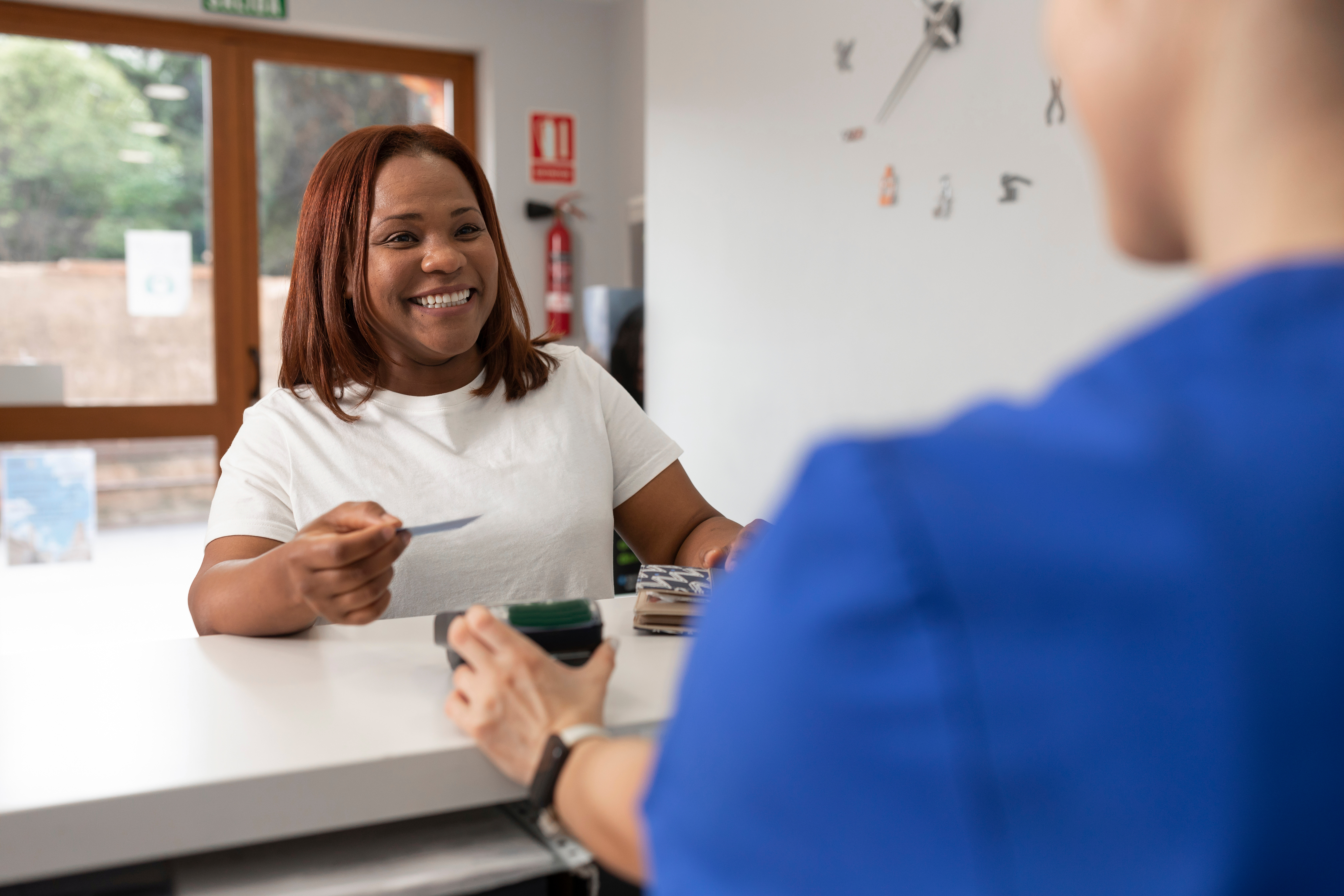 A smiling female patient holds a credit card up to a credit card reader to process a payment.