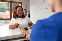 A smiling female patient holds a credit card up to a credit card reader to process a payment.