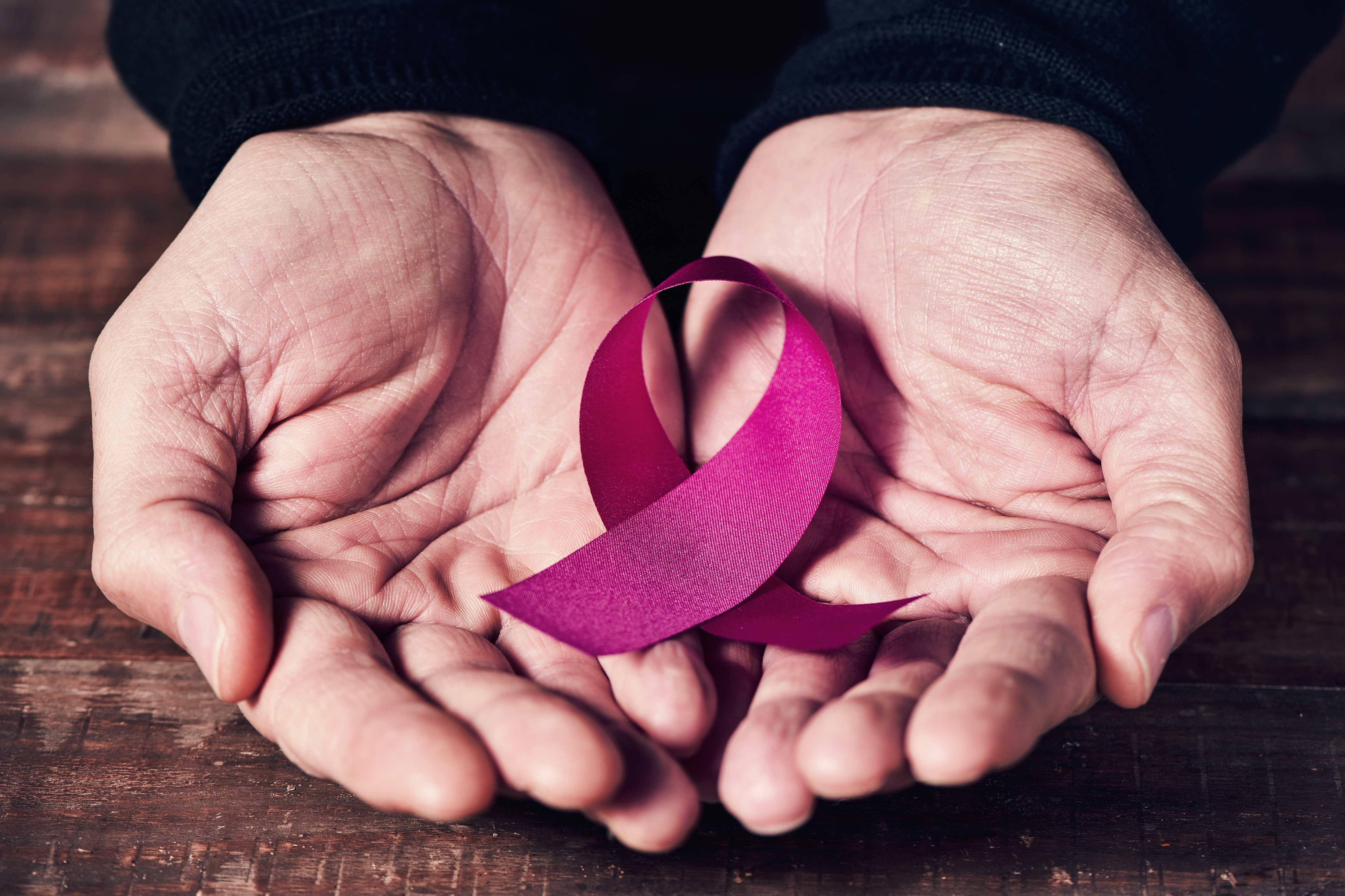 A woman's hands hold a pink ribbon. The pink ribbon symbolizes breast cancer awareness.