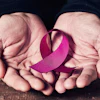 A woman's hands hold a pink ribbon. The pink ribbon symbolizes breast cancer awareness.