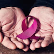 A woman's hands hold a pink ribbon. The pink ribbon symbolizes breast cancer awareness.