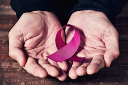 A woman's hands hold a pink ribbon. The pink ribbon symbolizes breast cancer awareness.