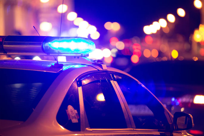 Police car with blue emergency lights activated at night with blurred city lights in the background.