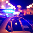 A police car is shown with its blue overhead lights illuminated at night with city lights in the background.