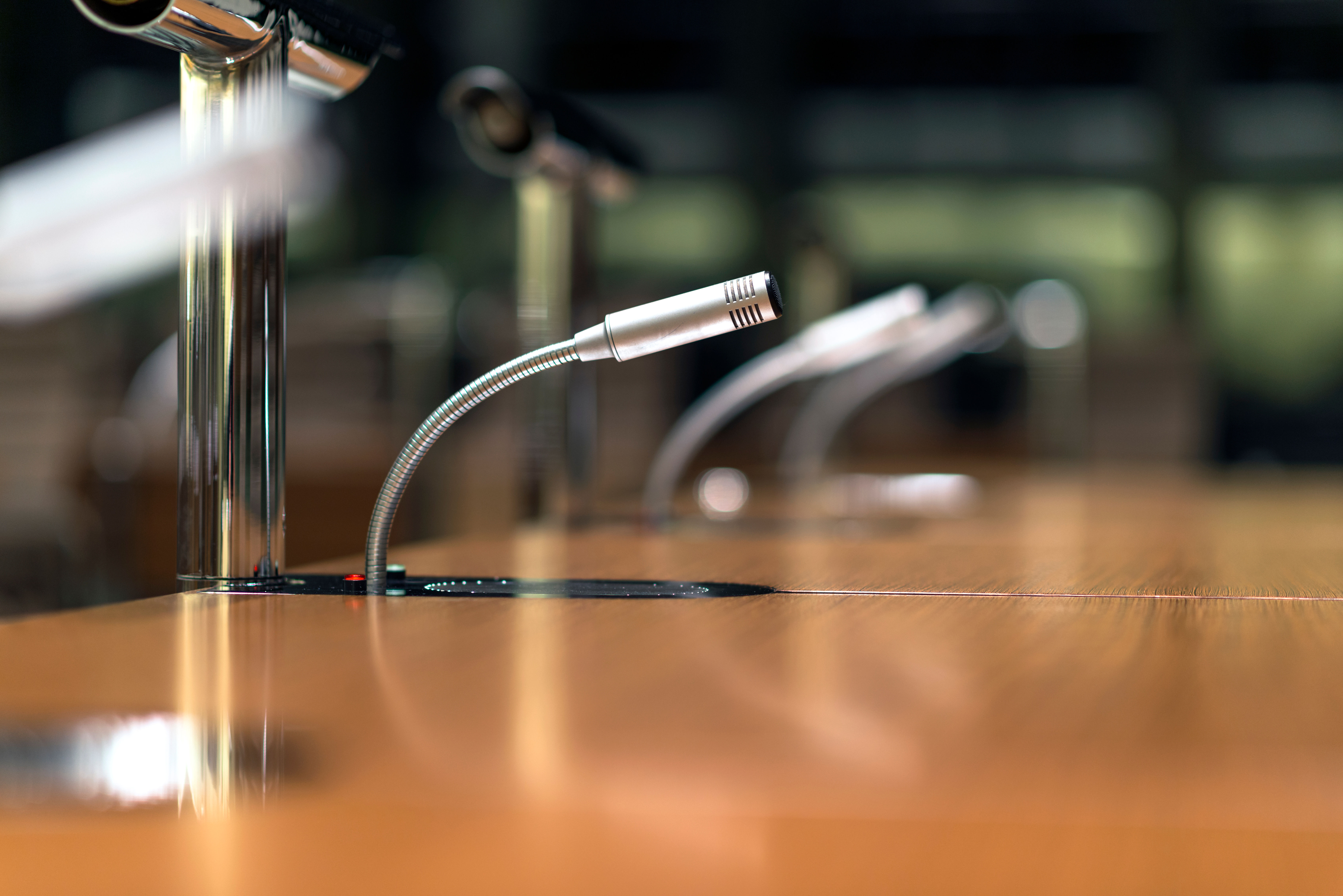 Professional microphones with flexible gooseneck stands on a wooden conference table.