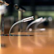 Professional microphones with flexible gooseneck stands on a wooden conference table.