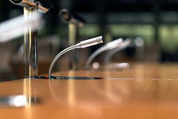 Professional microphones with flexible gooseneck stands on a wooden conference table.