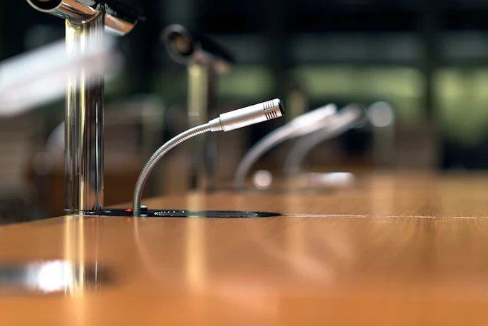 Professional microphones with flexible gooseneck stands on a wooden conference table.