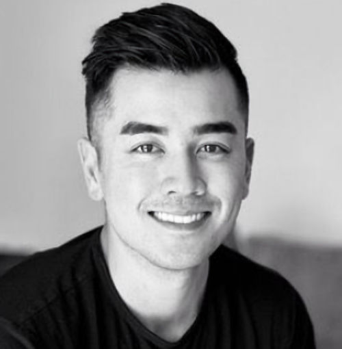 Professional black and white headshot of a smiling man with styled dark hair wearing a dark shirt