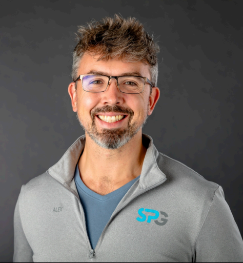 Professional headshot of smiling man with glasses wearing gray SPR-branded jacket over blue shirt