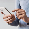 A man wearing a blue shirt holds a smartphone with his forefinger poised above the screen.