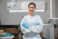 A woman wearing PPE smiles at the viewer. Behind her is a modern dental operatory.