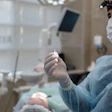 A dentist wearing a surgical mask and gloves holds a dental implant abutment.