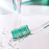 A hand holds a green-bristle toothbrush under running water.