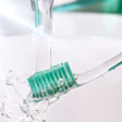 A hand holds a green-bristle toothbrush under running water.