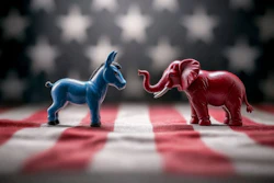 A blue donkey and red elephant face each other with an American flag in the background.