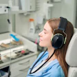 A woman dental patient has her eyes closed and has black headphones placed over her ears.
