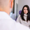 A woman sitting in a dental chair has a serious expression on her face while a dentist, who is in the foreground, talks to her.