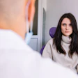 A woman sitting in a dental chair has a serious expression on her face while a dentist, who is in the foreground, talks to her.