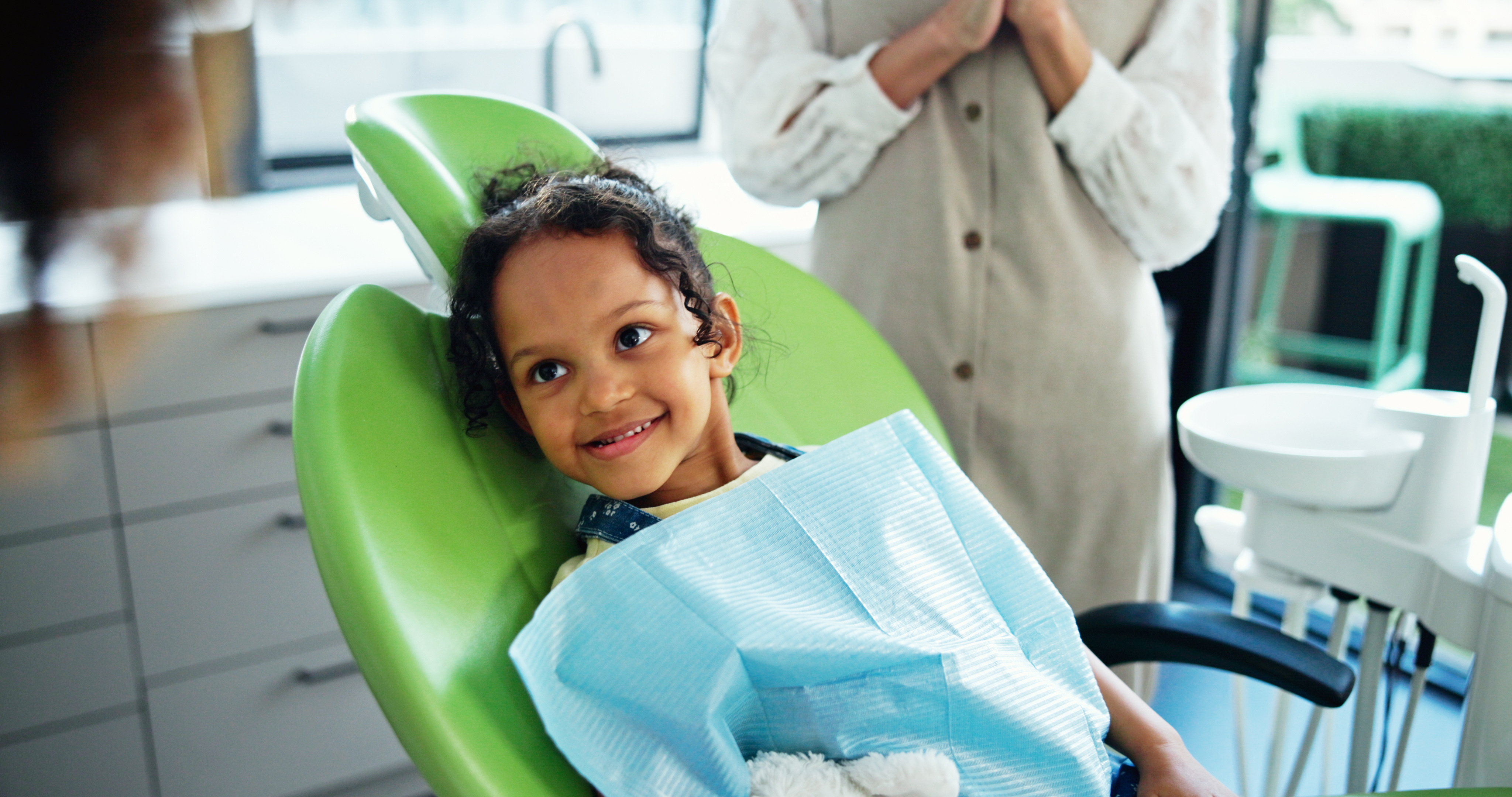 A young girl sits in a dental chair and smiles.