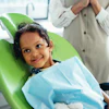 A young girl sits in a dental chair and smiles.