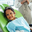 A young girl sits in a dental chair and smiles.