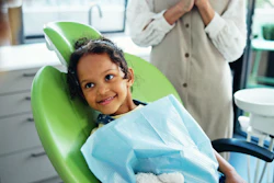 A young girl sits in a dental chair and smiles.